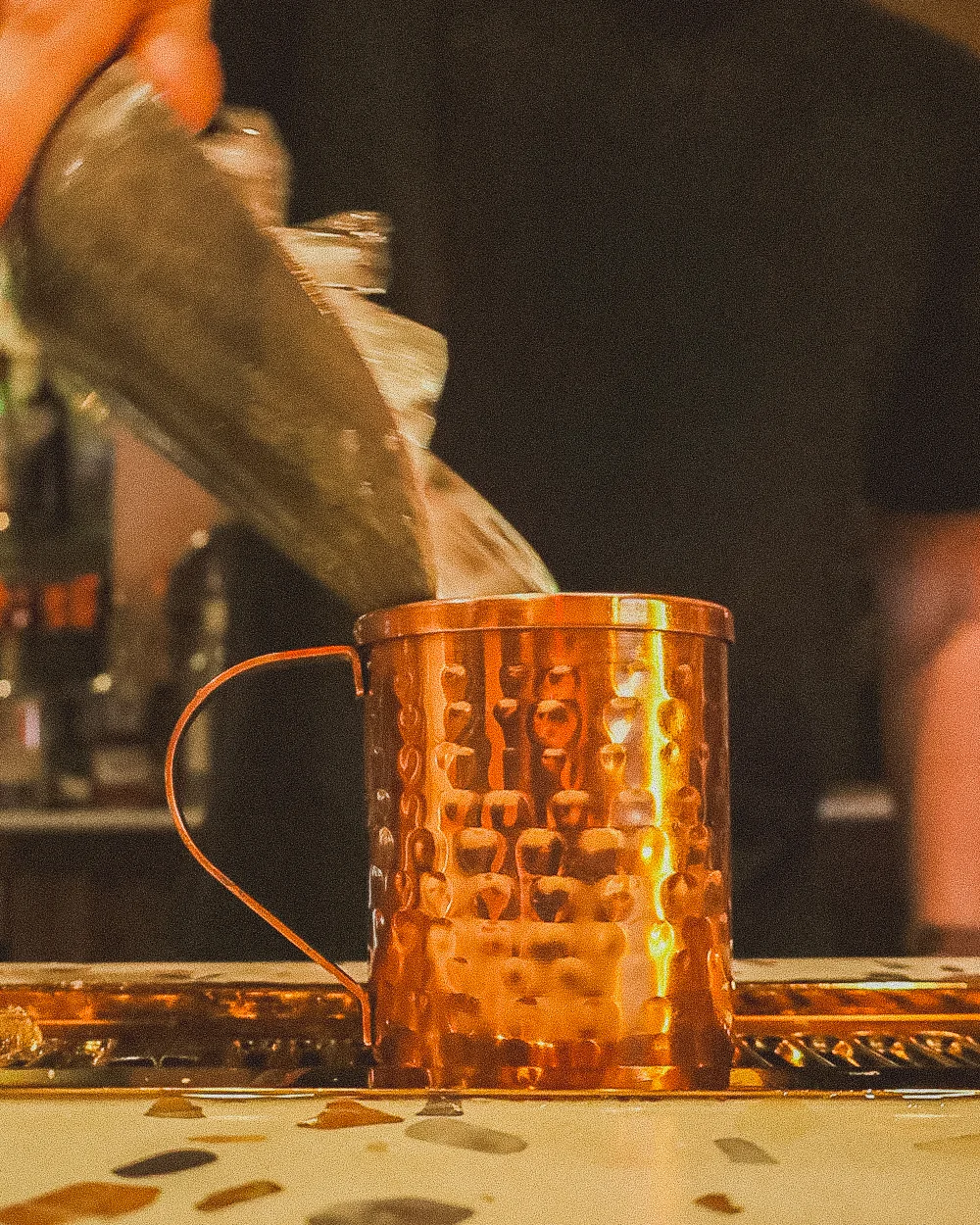 Bartender pouring drink into a copper mug at a bar.