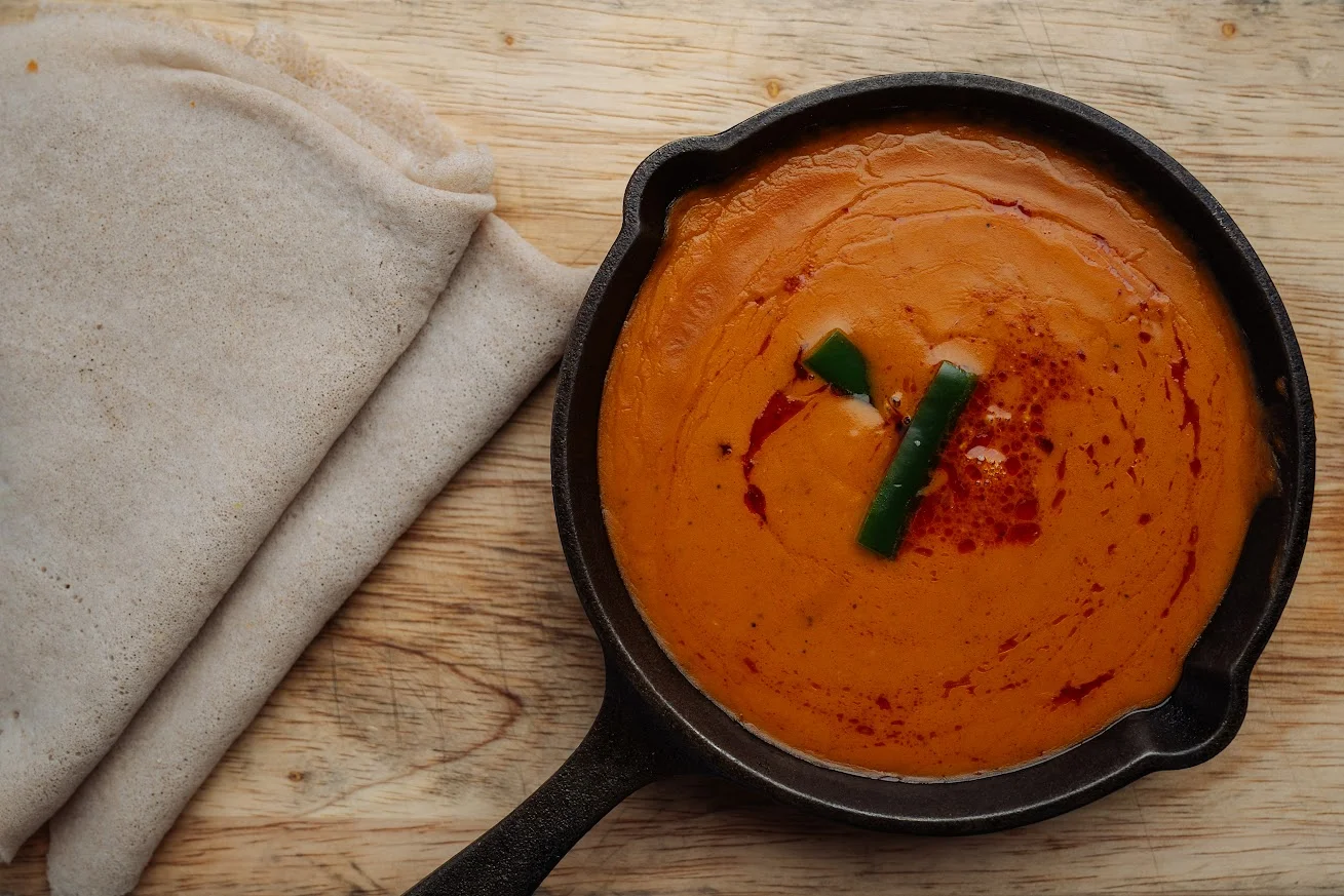 A bowl of smooth, spiced sauce with a swirl of red oil, accompanied by traditional flatbreads.