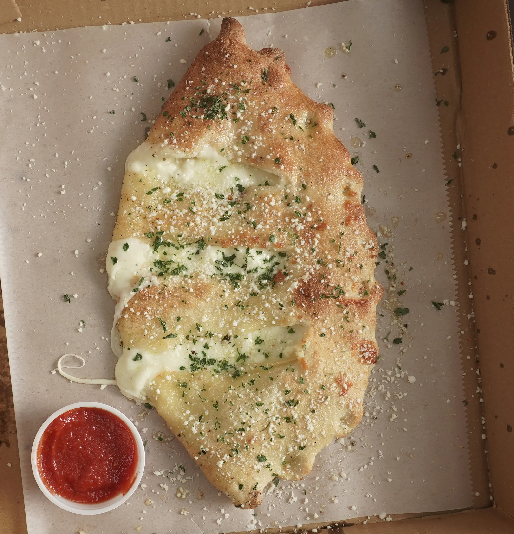 A cheese calzone topped with parsley and a side of marinara sauce. 