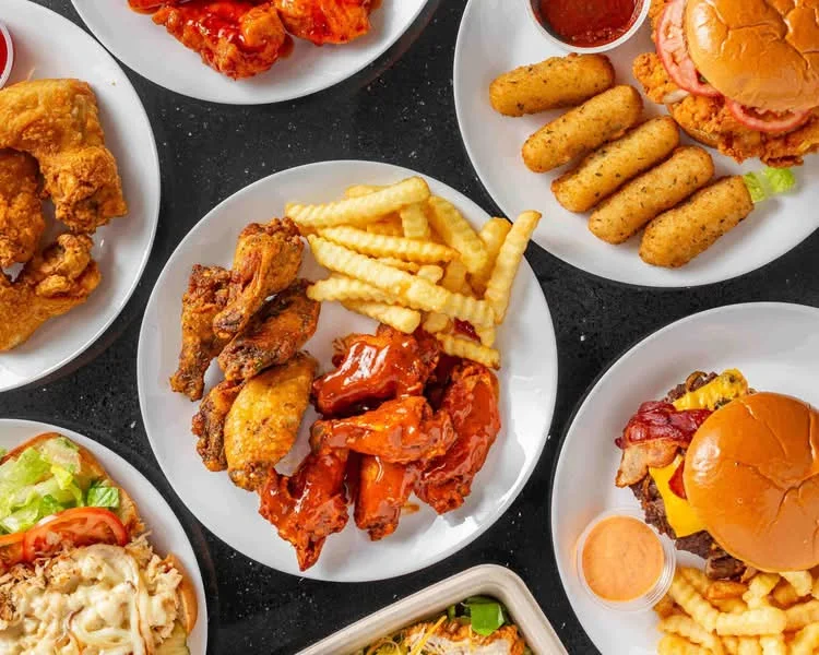 An assortment of delicious dishes including fried chicken, buffalo wings, fries, mozzarella sticks, and burgers, all served on white plates.