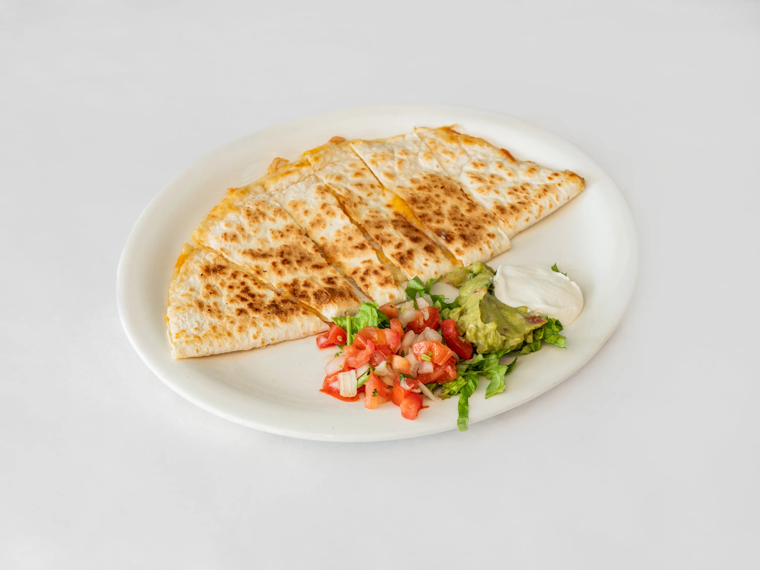 A plate featuring a quesadilla cut into wedges, served with guacamole, sour cream, and diced tomatoes.