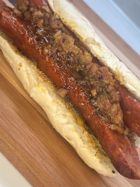 A hot dog in a bun topped with a savory mixture, presented on a wooden surface.