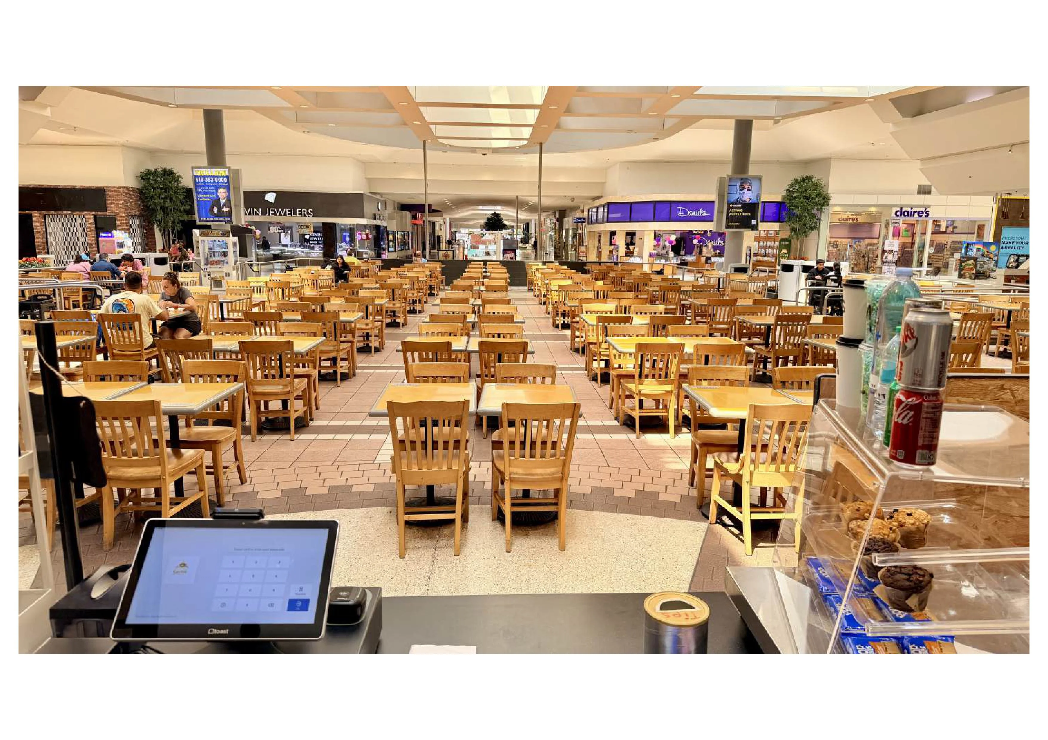Empty food court with wooden tables and chairs in a mall setting.