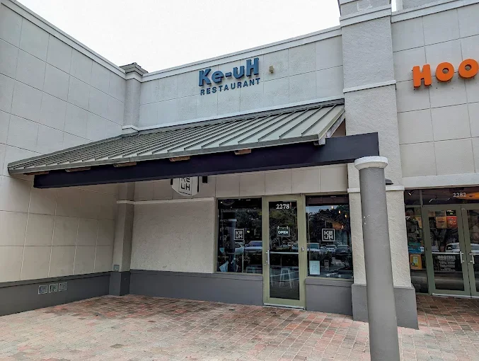 The exterior storefront of Ke-uH Weston featuring a modern blue sign and glass entrance under a large metal awning.