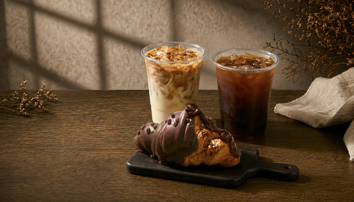 Iced coffee drinks and a chocolate croissant on a wooden table