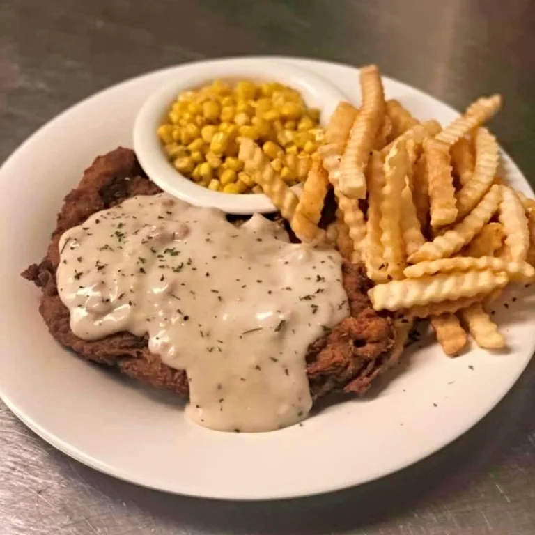 A toasted chicken salad sandwich with a creamy filling, served with a side of golden crinkle-cut fries on a white plate.