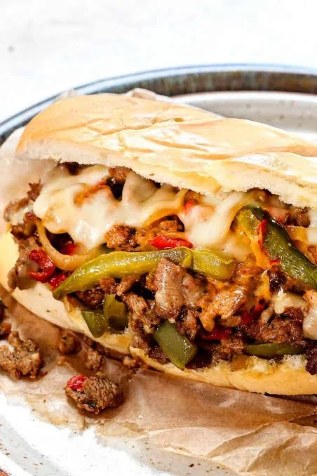 A sandwich featuring savory grilled meat, bell peppers, and melted cheese in a soft sub roll.