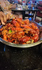 A large bowl filled with bright red lobsters, mixed with spices and garnishes, being served at a seafood restaurant.