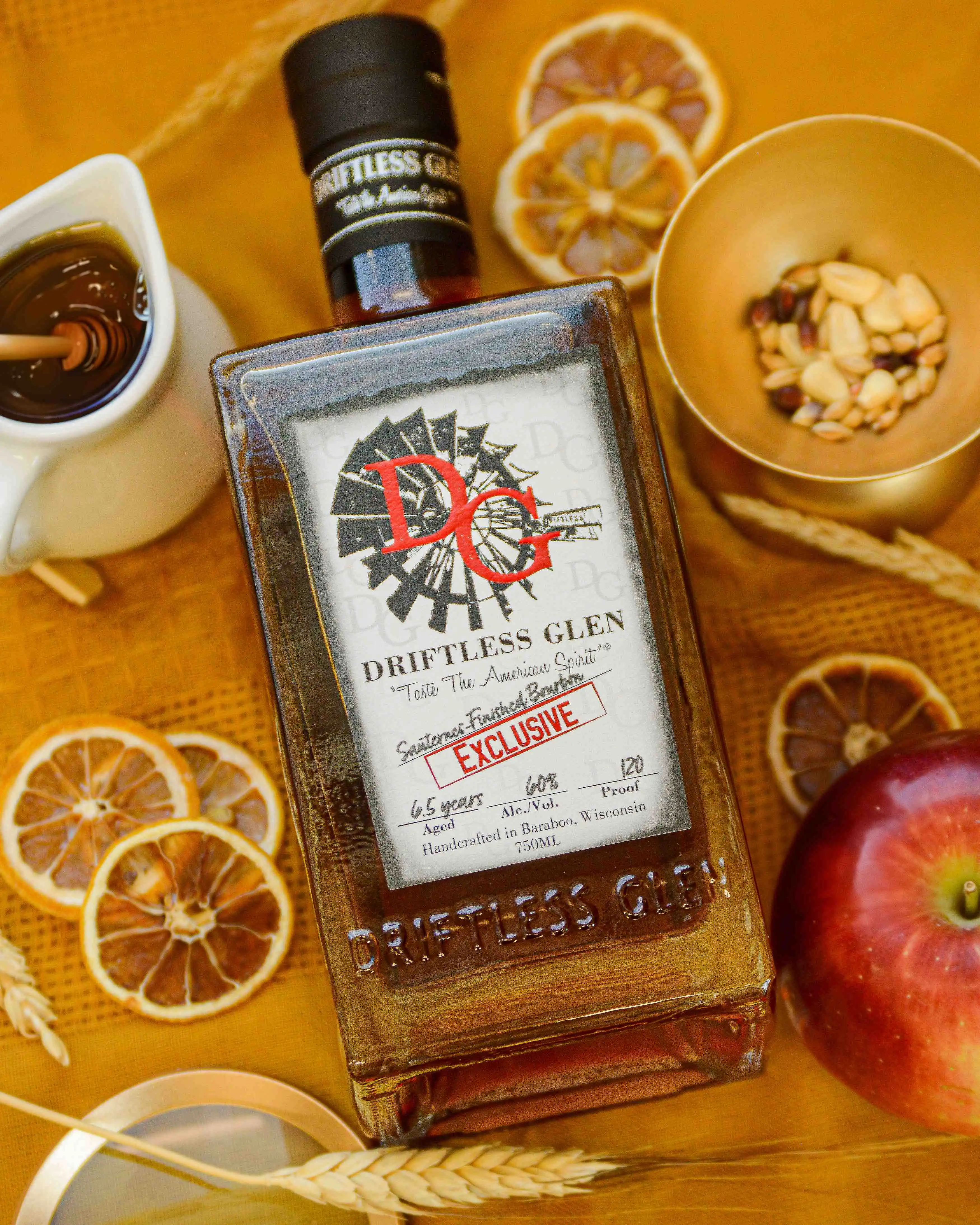 A bottle of Sauternes-Finished Bourbon sits with honey, grain, and dried fruit on a yellow backdrop.