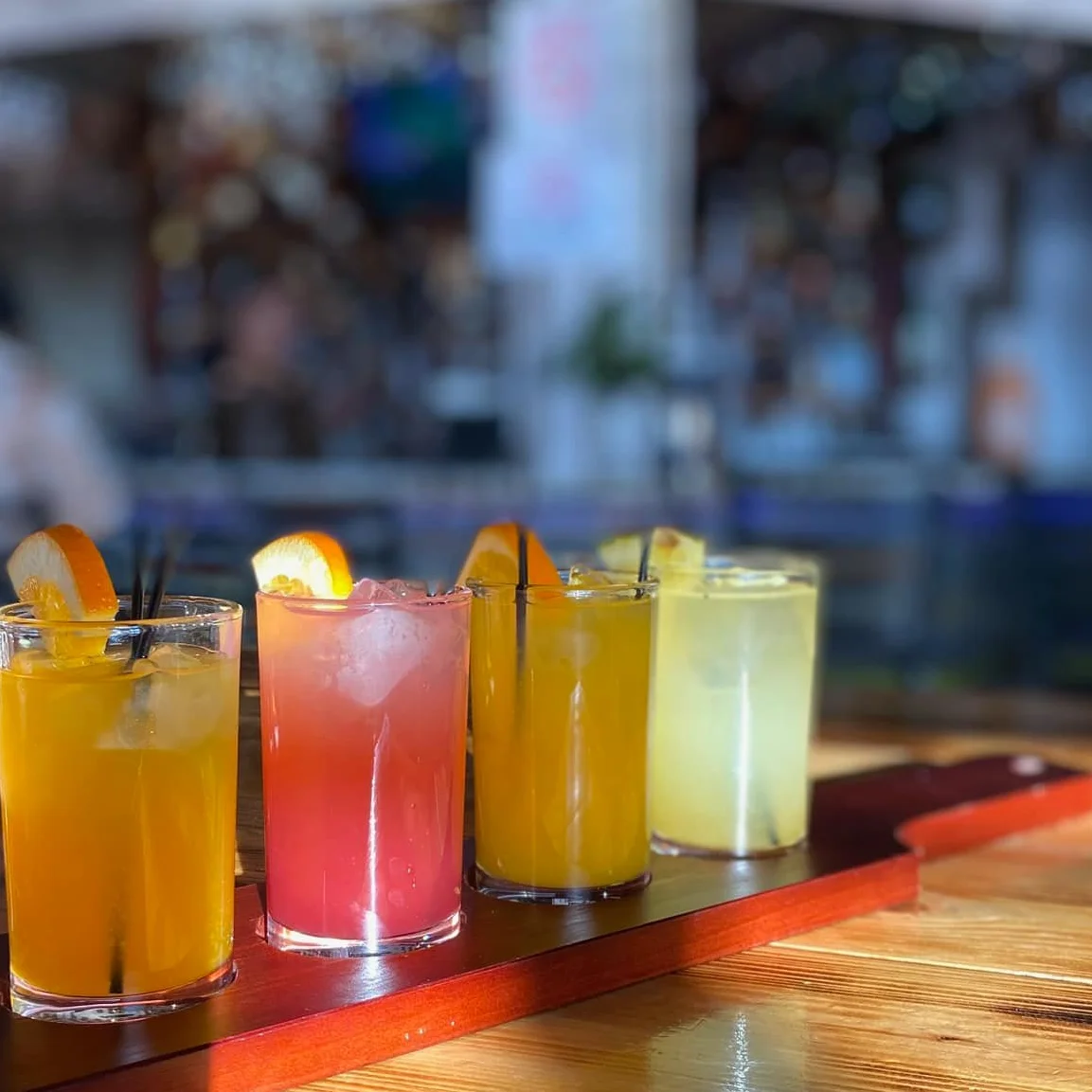 Colorful cocktail flight with four refreshing drinks on a wooden tray