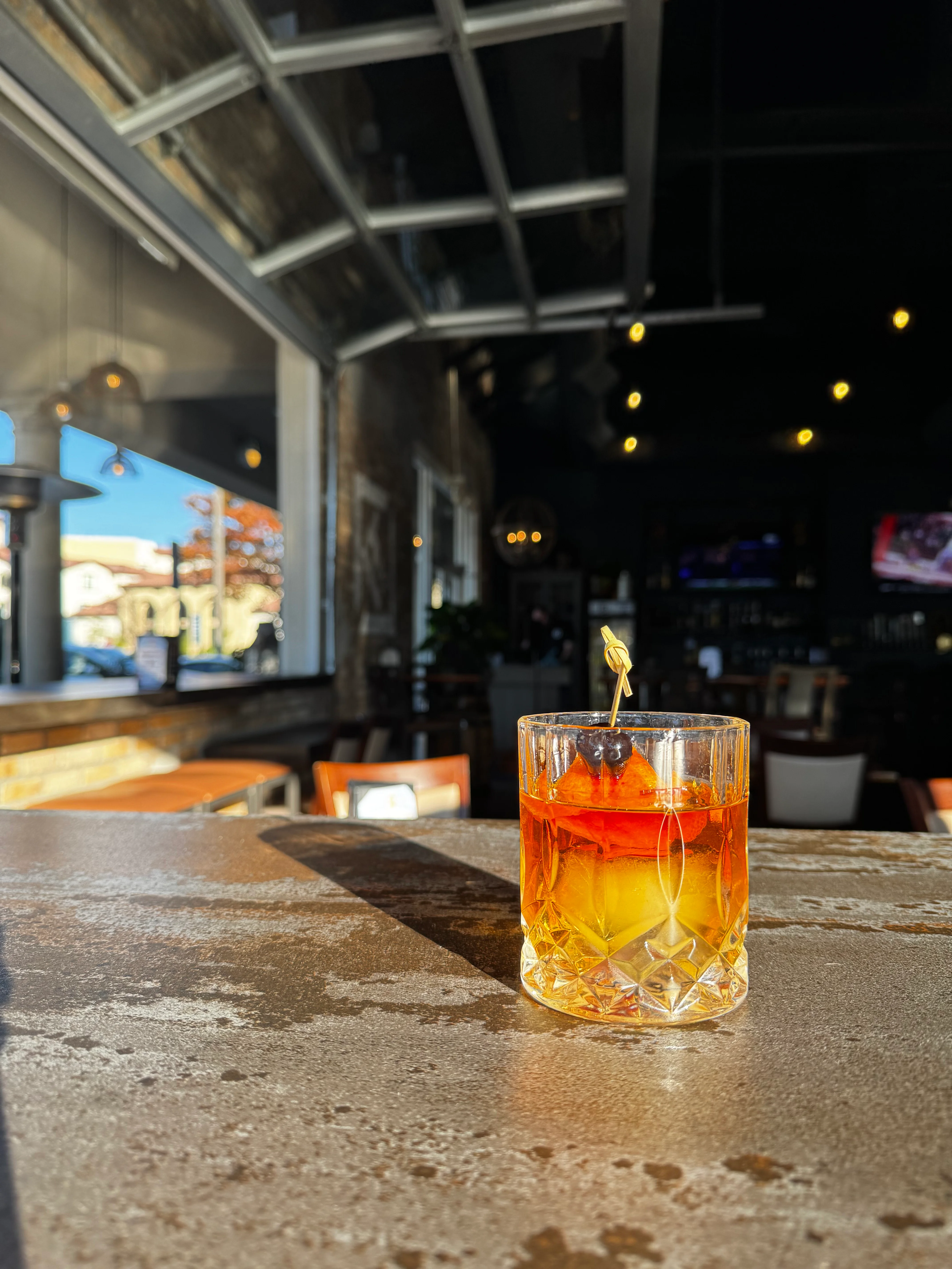 Craft cocktail with cherry and orange garnish in a modern bar setting