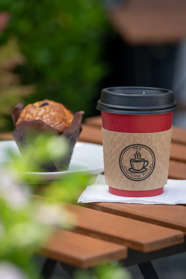 A coffee cup and muffin displayed on a table, with greenery in the background.