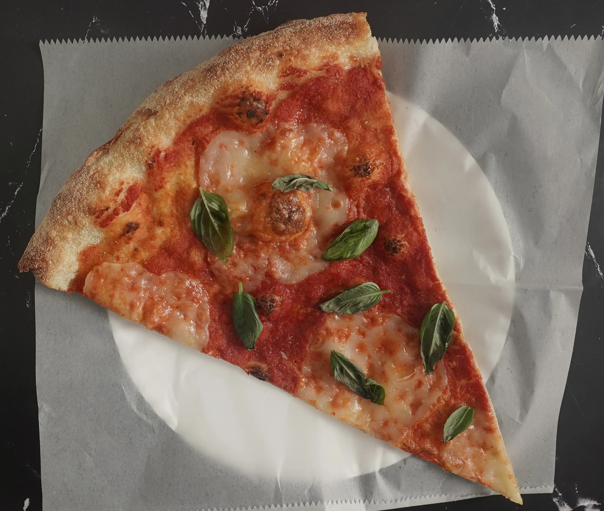 A Margherita pizza slice topped with fresh basil, EVOO, and marinara done the NY Style Way.