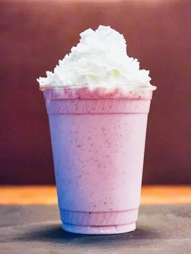 A cup filled with a creamy pink milkshake topped with a generous amount of whipped cream.