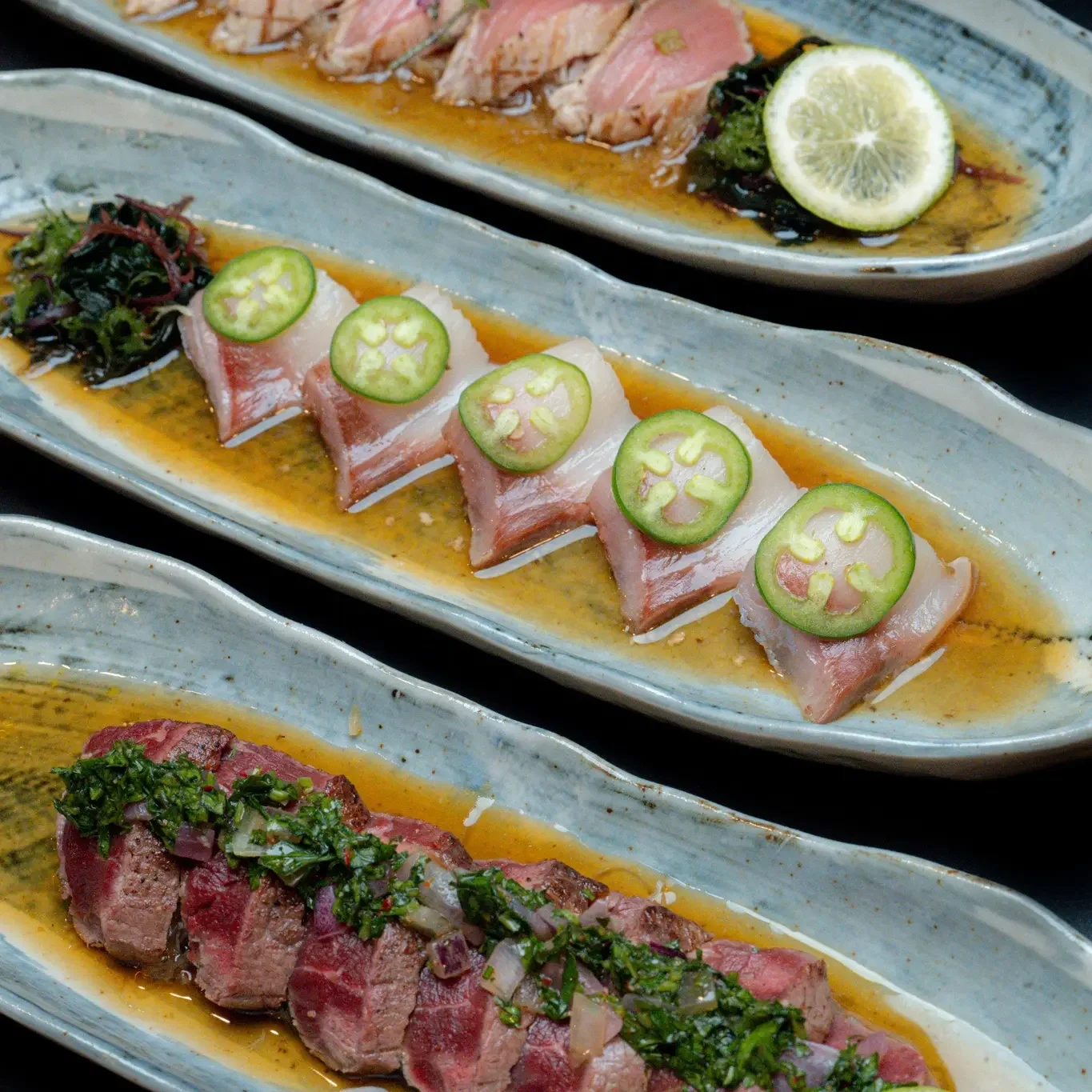 Three elegant sushi plates, showcasing various styles of sushi with fish and garnishes, served with a slice of lemon.