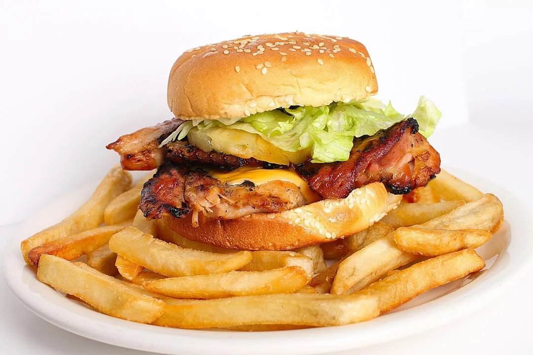 A grilled chicken sandwich with lettuce and pineapple, served with a side of golden French fries.