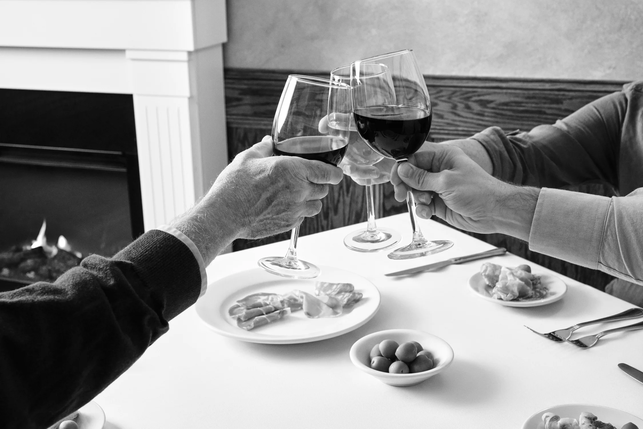 Cheers with wine glasses at a dining table with appetizers.