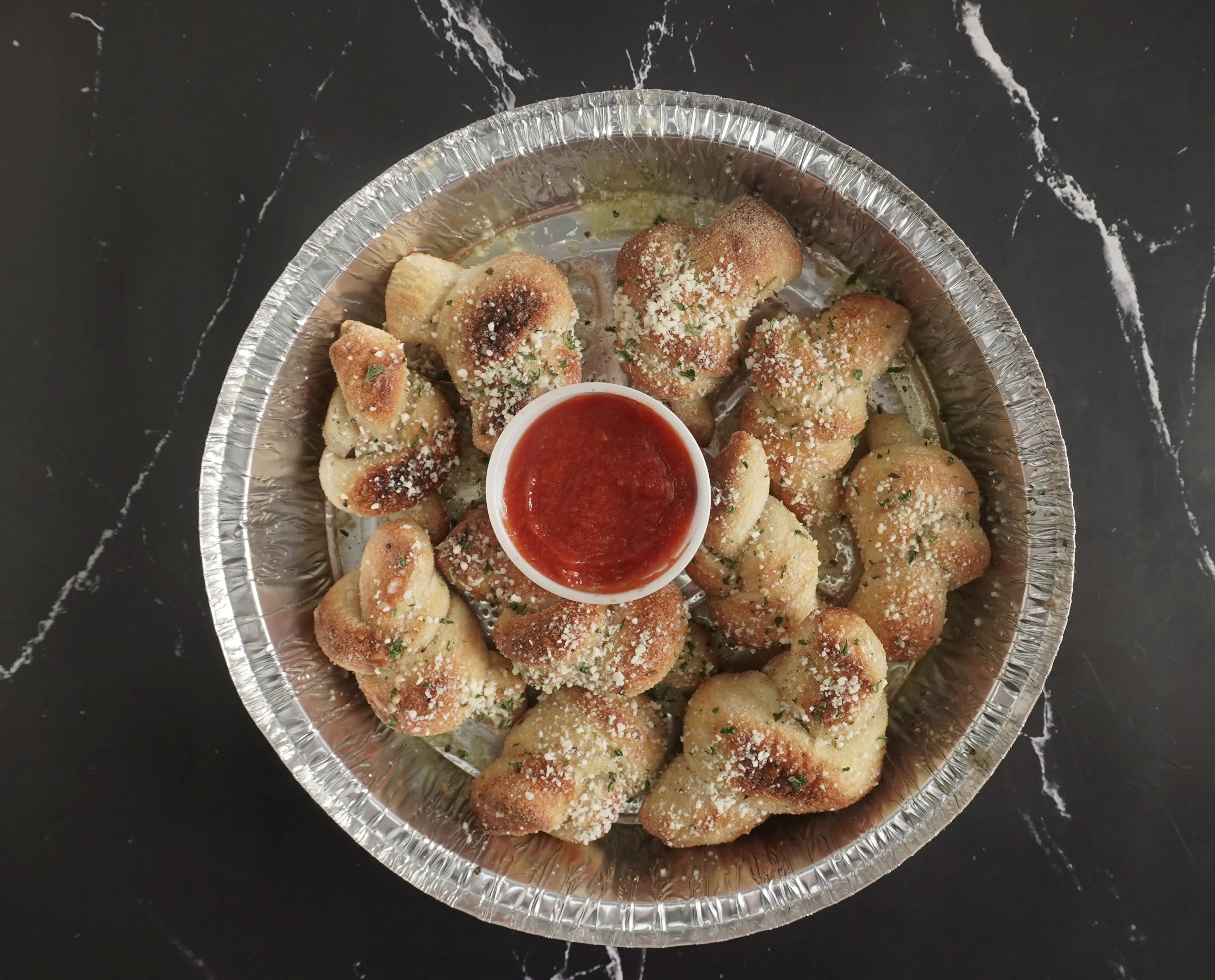 Golden garlic knots topped with parsley on a white plate.