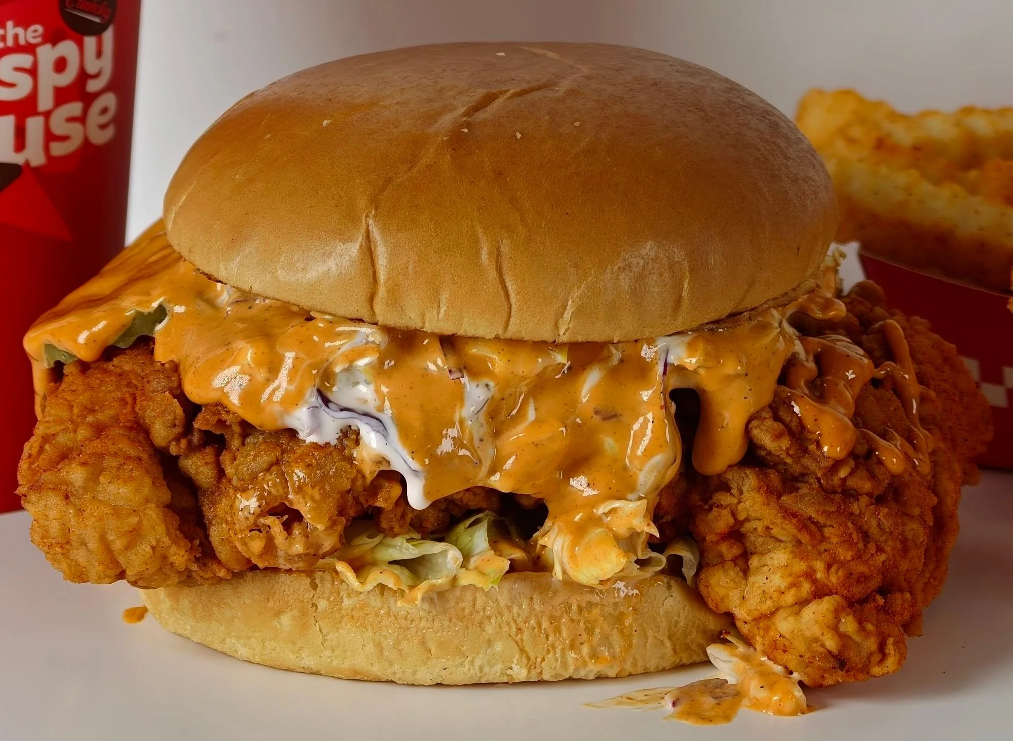 A hearty chicken sandwich overflowing with crispy chicken, sauce, and a soft bun, served alongside fries.
