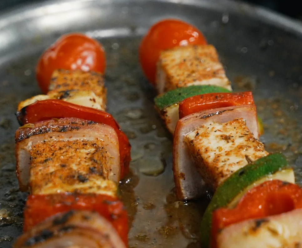 Grilled vegetable and tofu skewers on a metal tray.