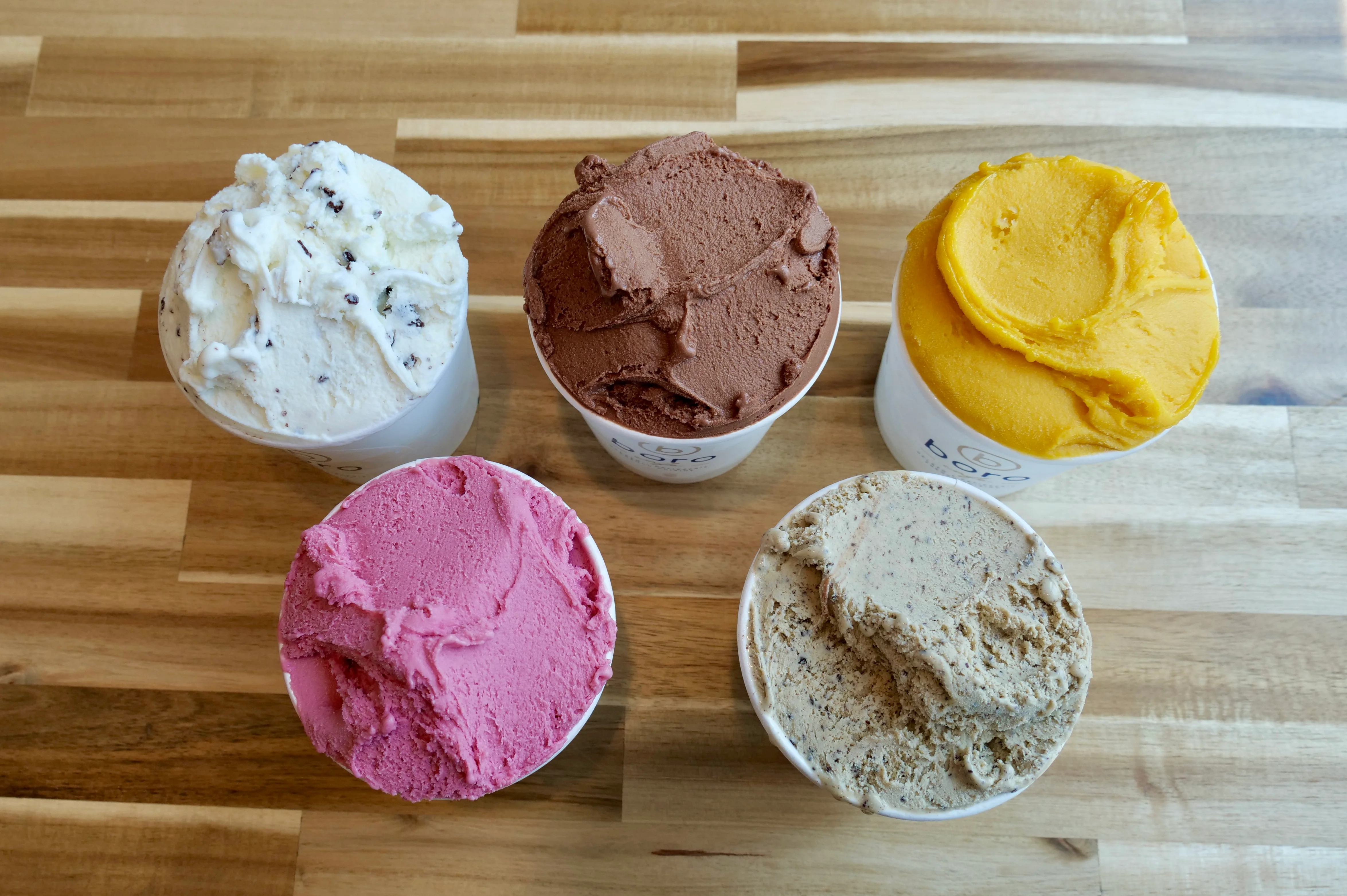 Assorted gelato flavors in cups on a wooden table