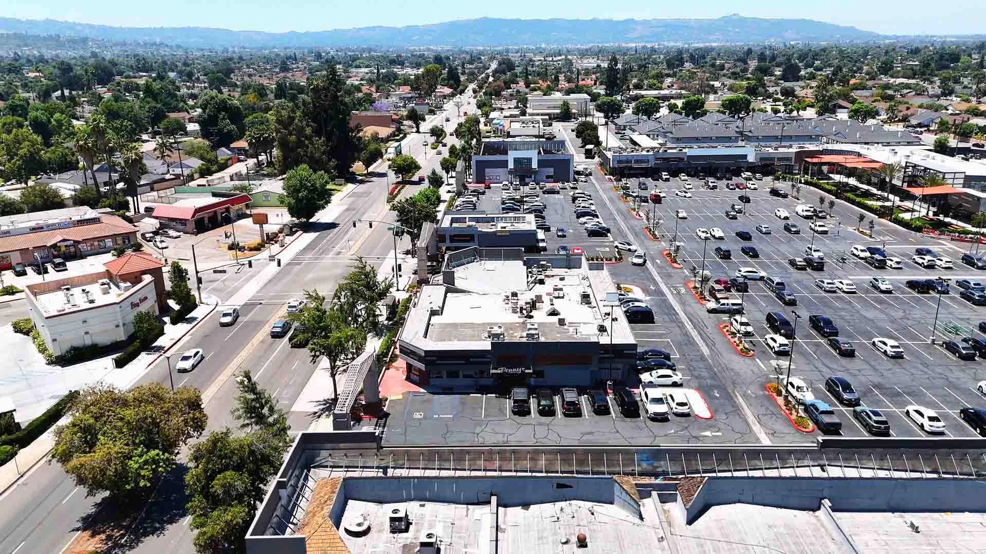 Aerial view of a shopping area with parking and surrounding greenery.