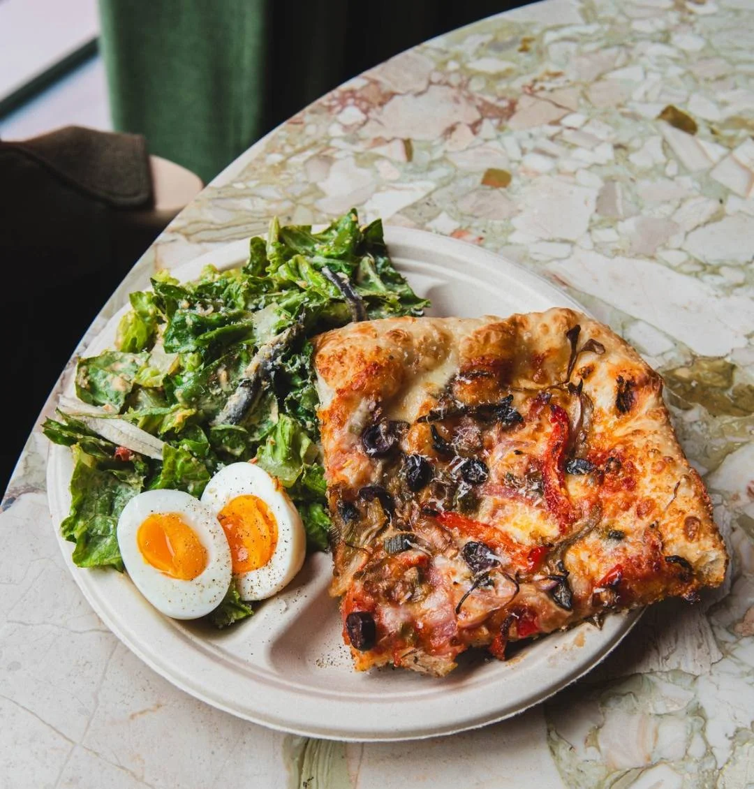 An appetizing plate featuring a slice of pizza topped with vegetables, served alongside a fresh salad and two soft-boiled eggs.