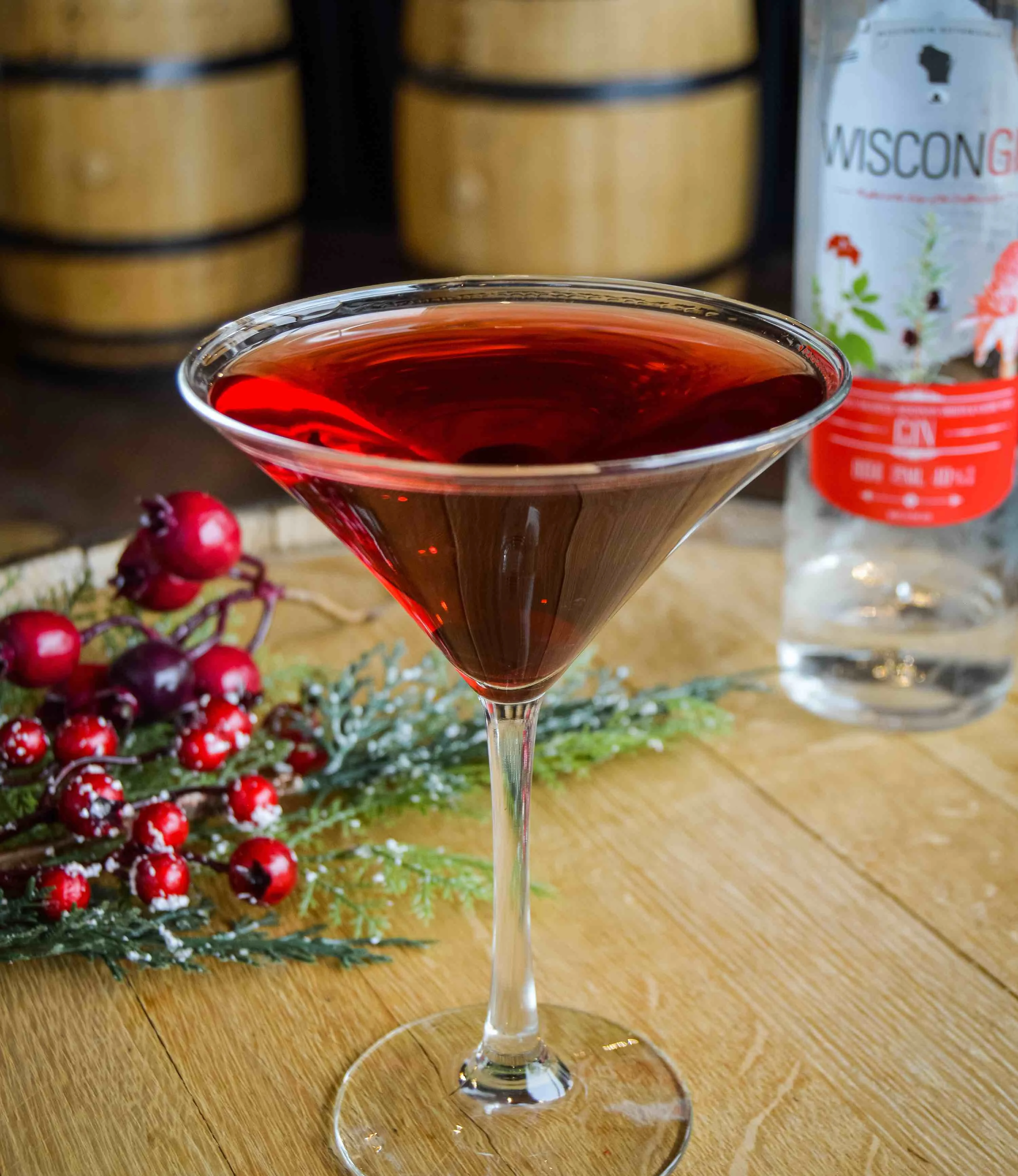 Wis-Cran-Gin Martini in front of a bottle of Driftless Glen's WisconGin with snowy cranberries in the background