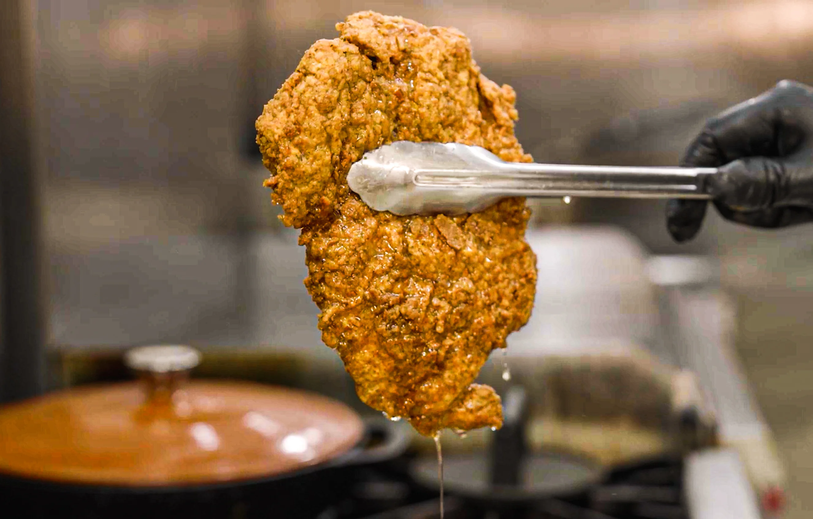 Crispy fried chicken cutlet on tongs