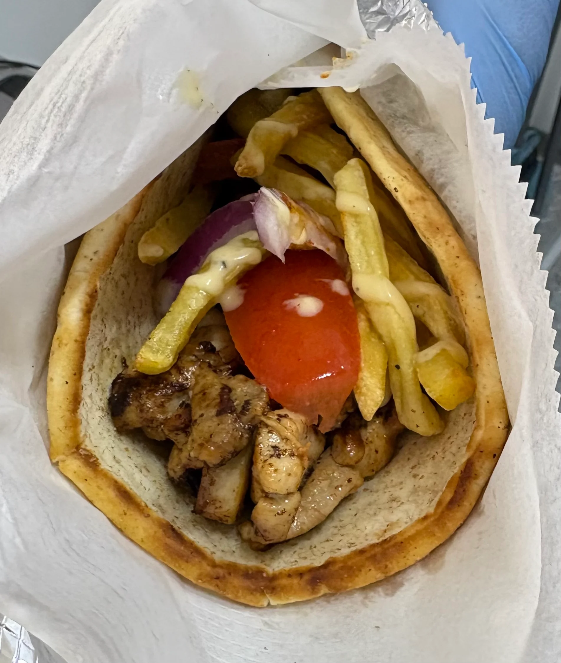 A pita-like bread filled with scrambled eggs, green bell peppers, tomato slices, and onions, wrapped in foil.