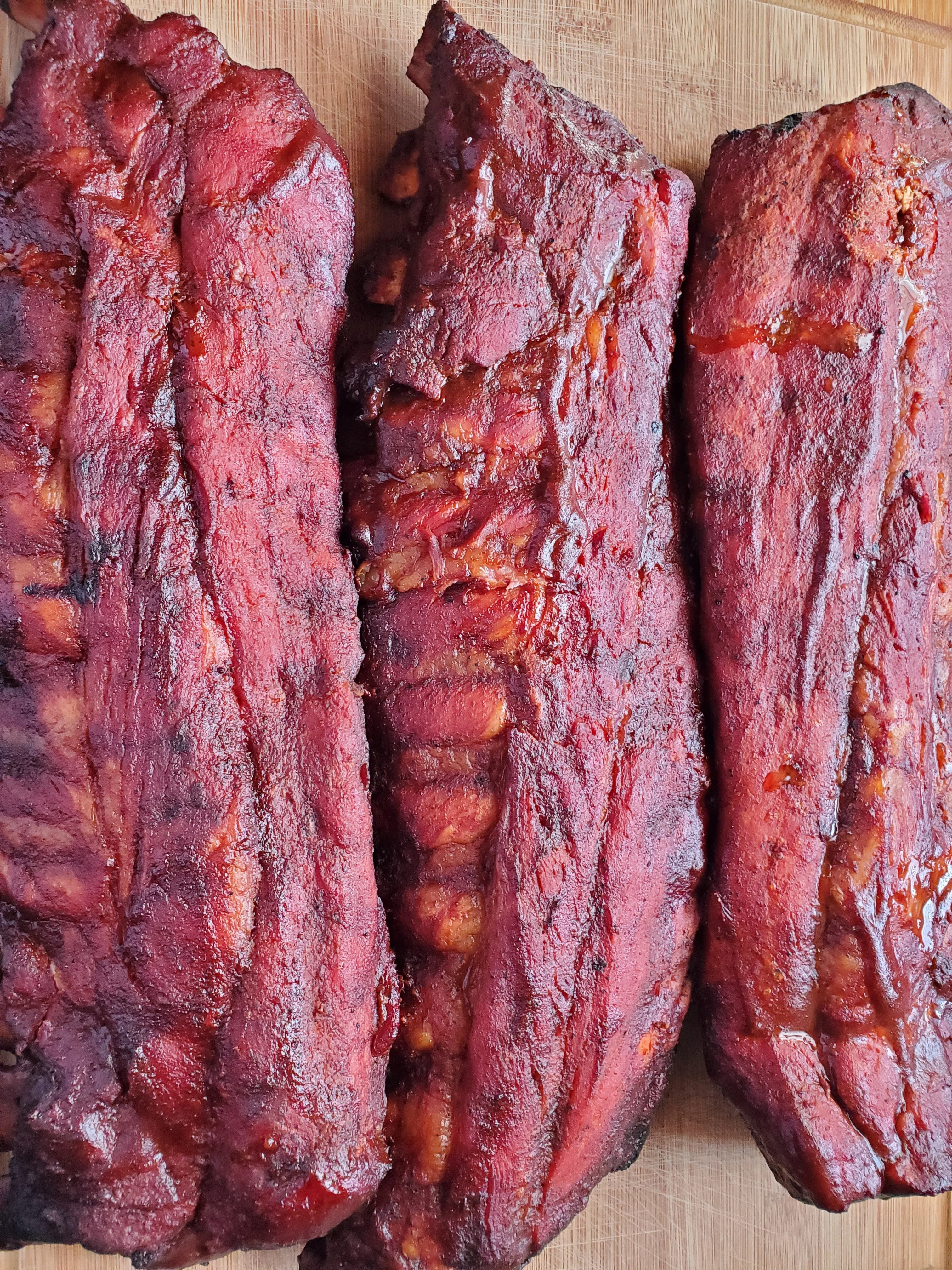 A close-up view of three succulent barbecue ribs, showcasing a rich glaze and smoky texture.