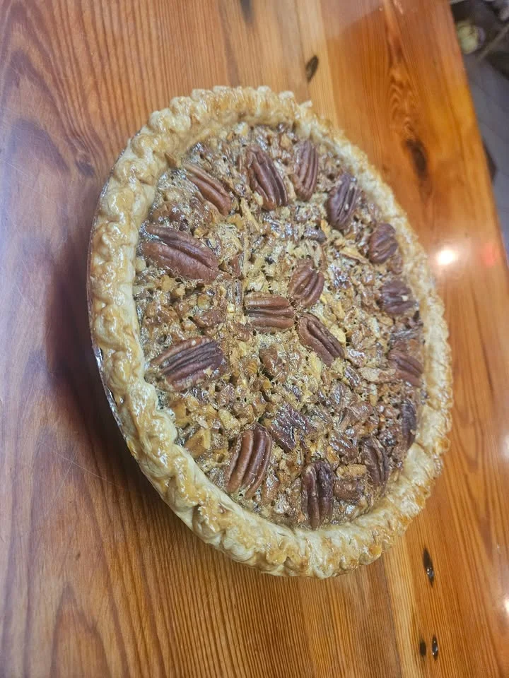A pecan pie with a golden-brown flaky crust, topped with pecans and a glossy filling, displayed on a wooden surface.