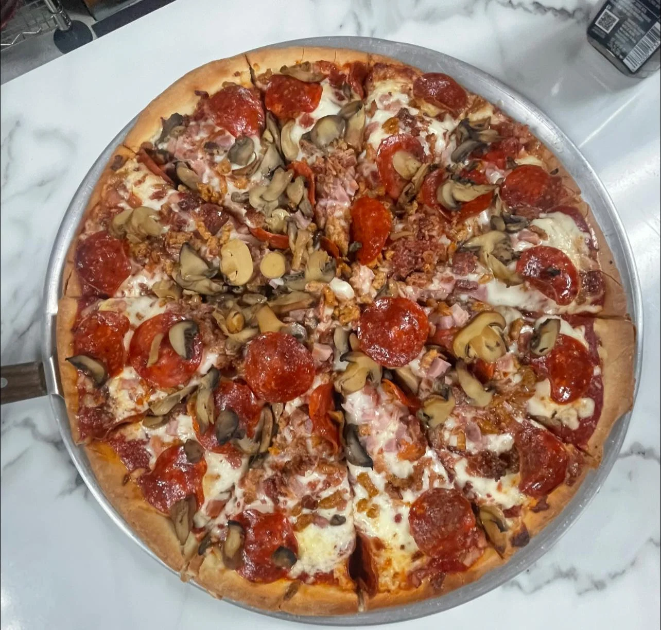 A delicious pizza topped with pepperoni, mushrooms, and various meats, displayed on a round tray.