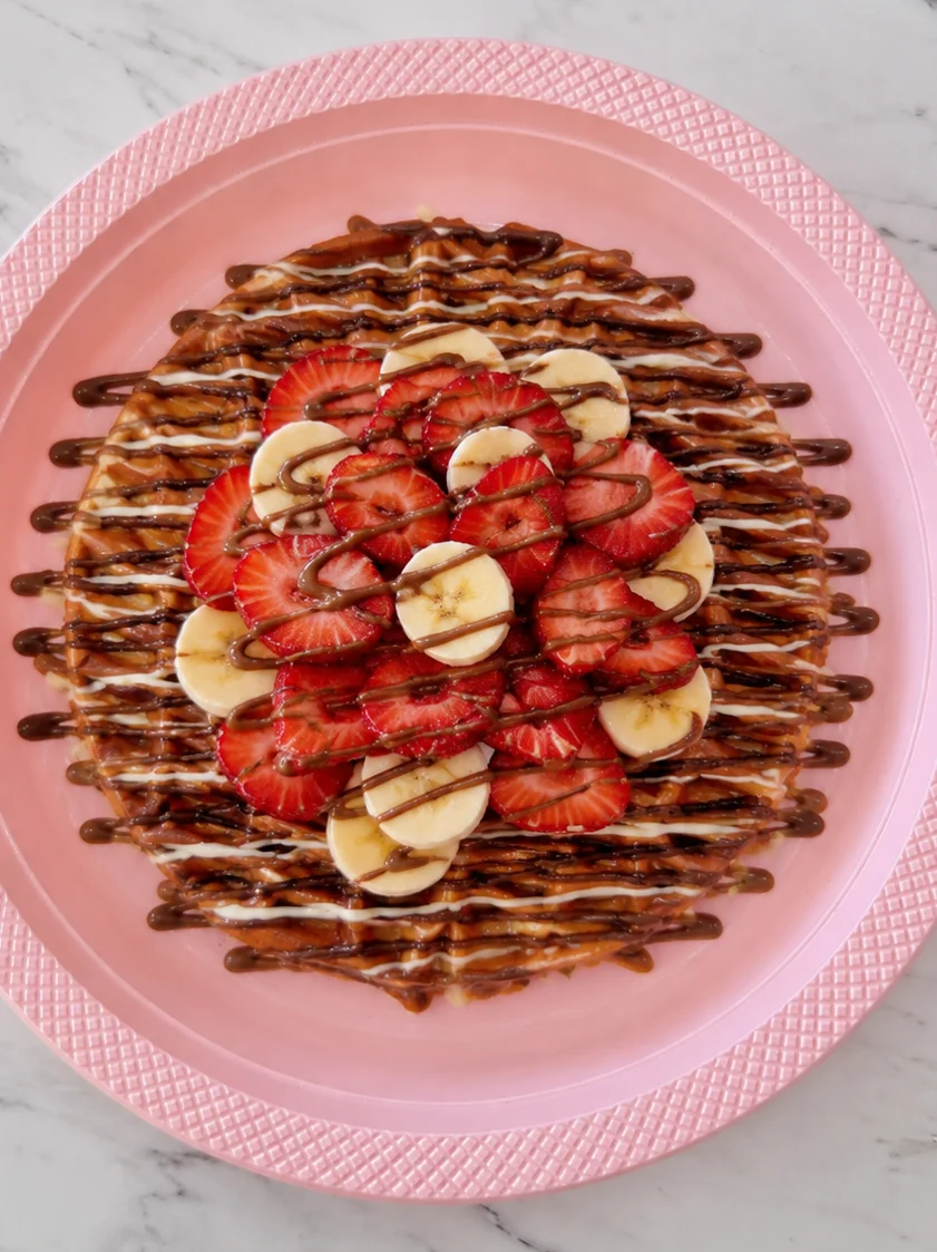 Delicious waffle topped with strawberries, bananas, and chocolate drizzle.