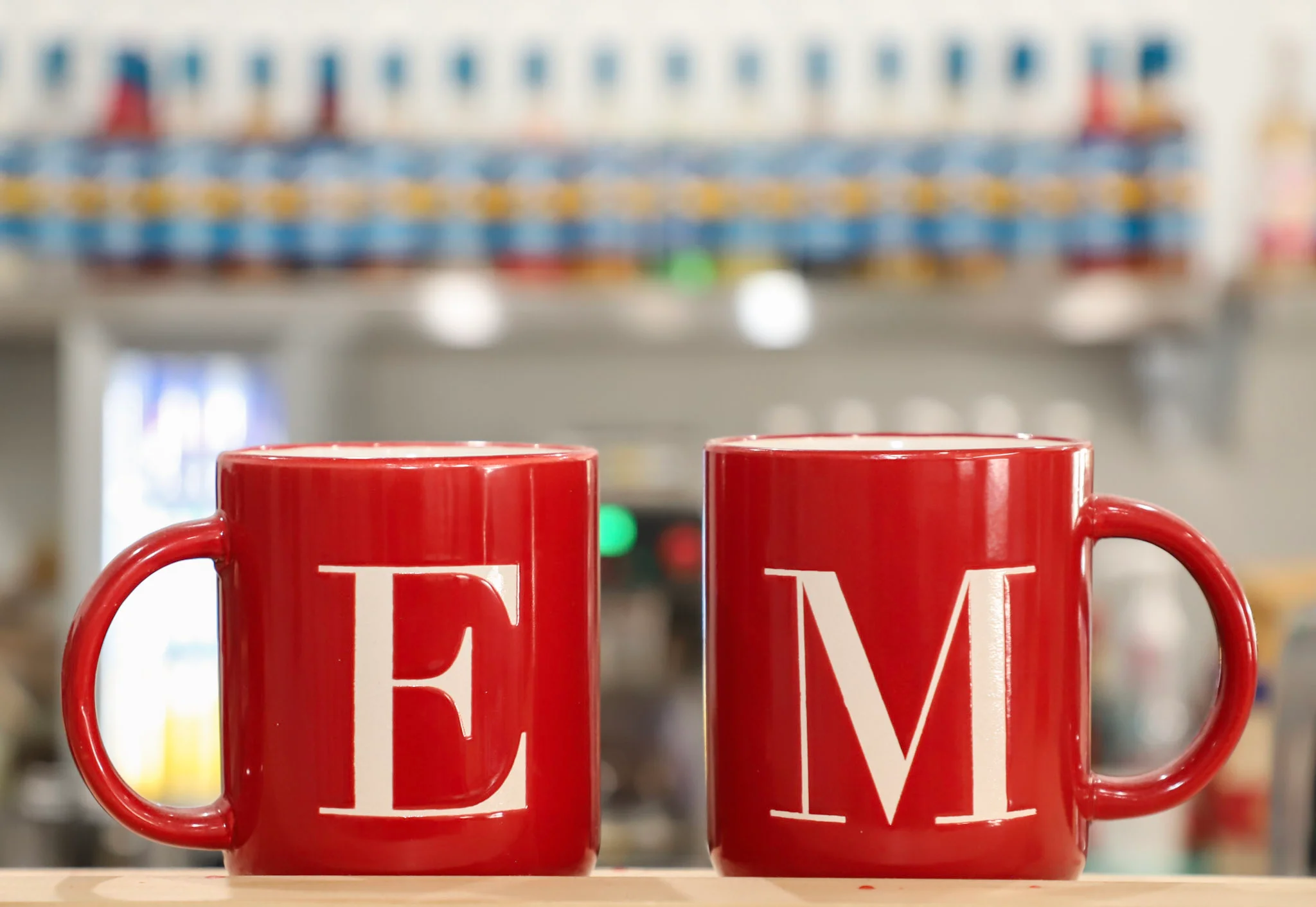 Two red mugs with letters E and M on a cafe counter