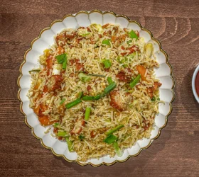 A plate of fried rice mixed with vegetables and herbs, garnished with green onions and served alongside a small bowl of sauce.