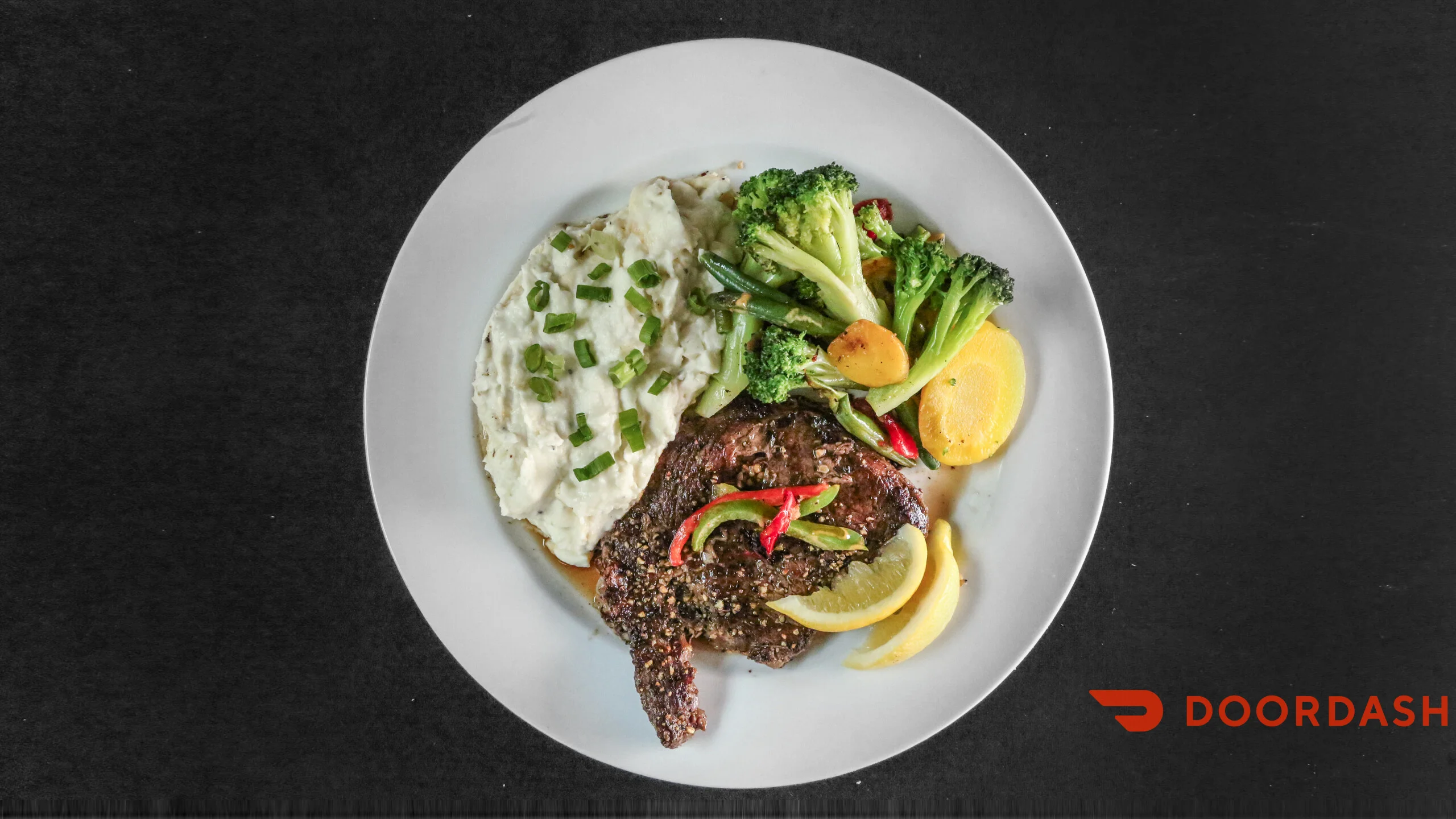 A plate featuring grilled steak, mashed potatoes, and mixed vegetables, garnished with lemon and green onions.