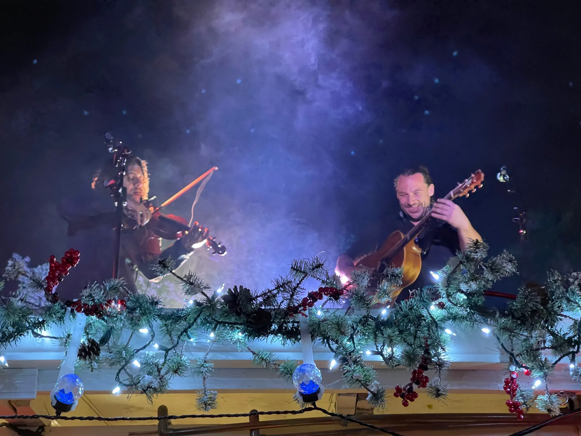 Musicians performing with violin and guitar under festive lights