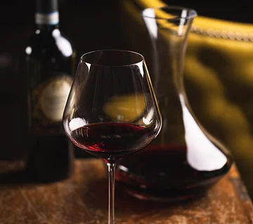 Elegant red wine glass with decanter and bottle on a wooden table
