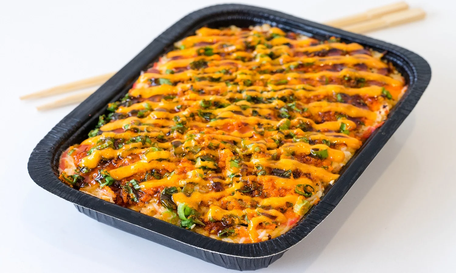 Baked dish topped with cheese, green onions, and sauce in a black tray.
