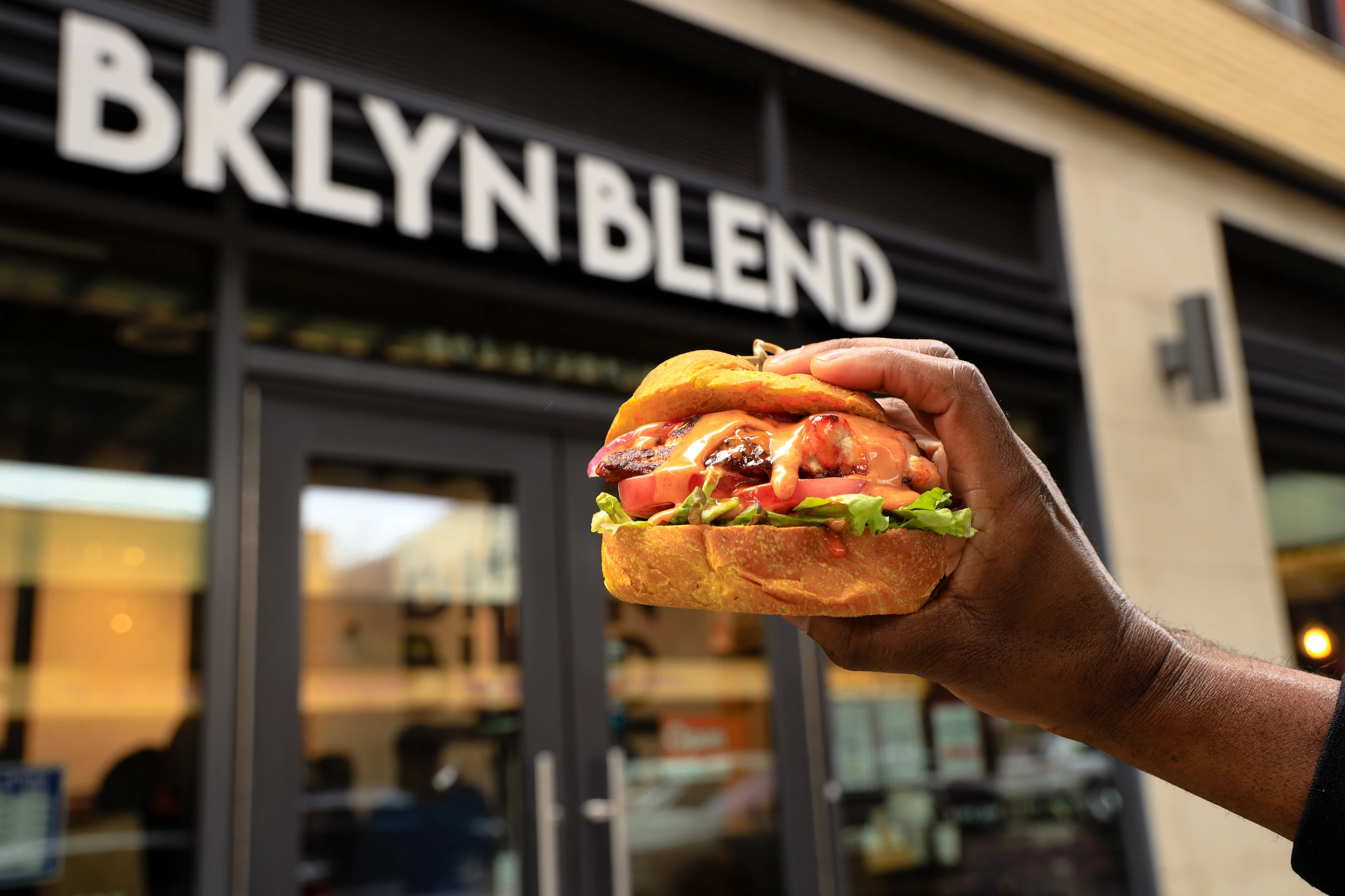 Handheld gourmet burger outside BKLYN BLEND restaurant