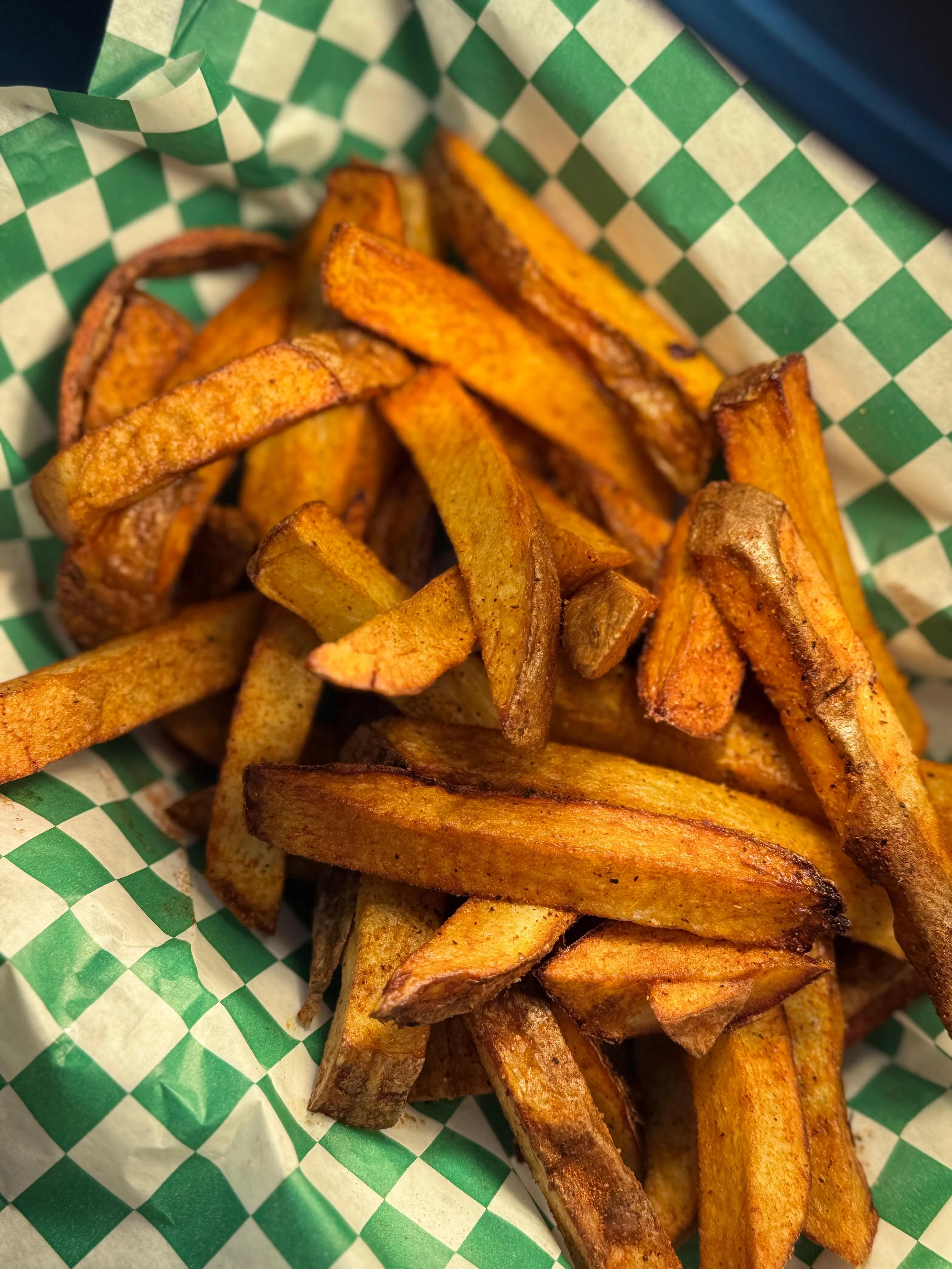 A basket filled with golden brown sweet potato fries arranged neatly on green and white checked paper.