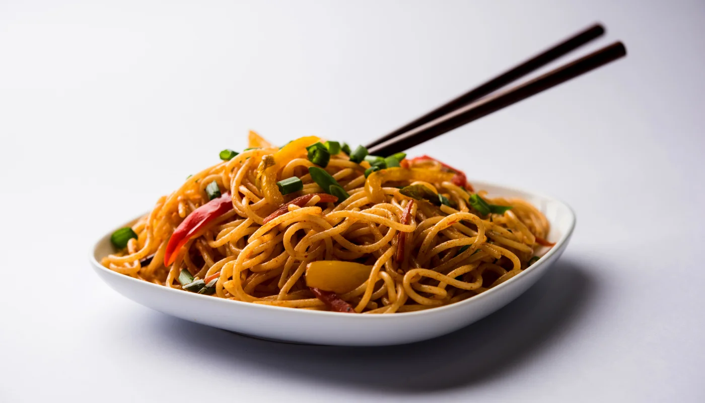 Plate of colorful Hakka noodles with vegetables and spices.