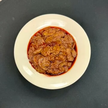 A plate of sweetened and syrupy bananas served in a thick sauce, placed in a white bowl.