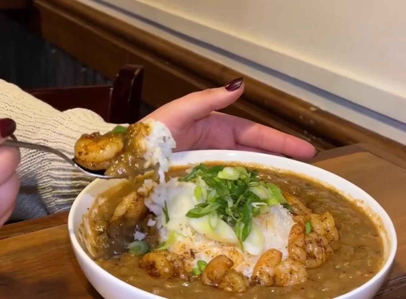 A bowl of shrimp and rice topped with green onions, served in a savory sauce.