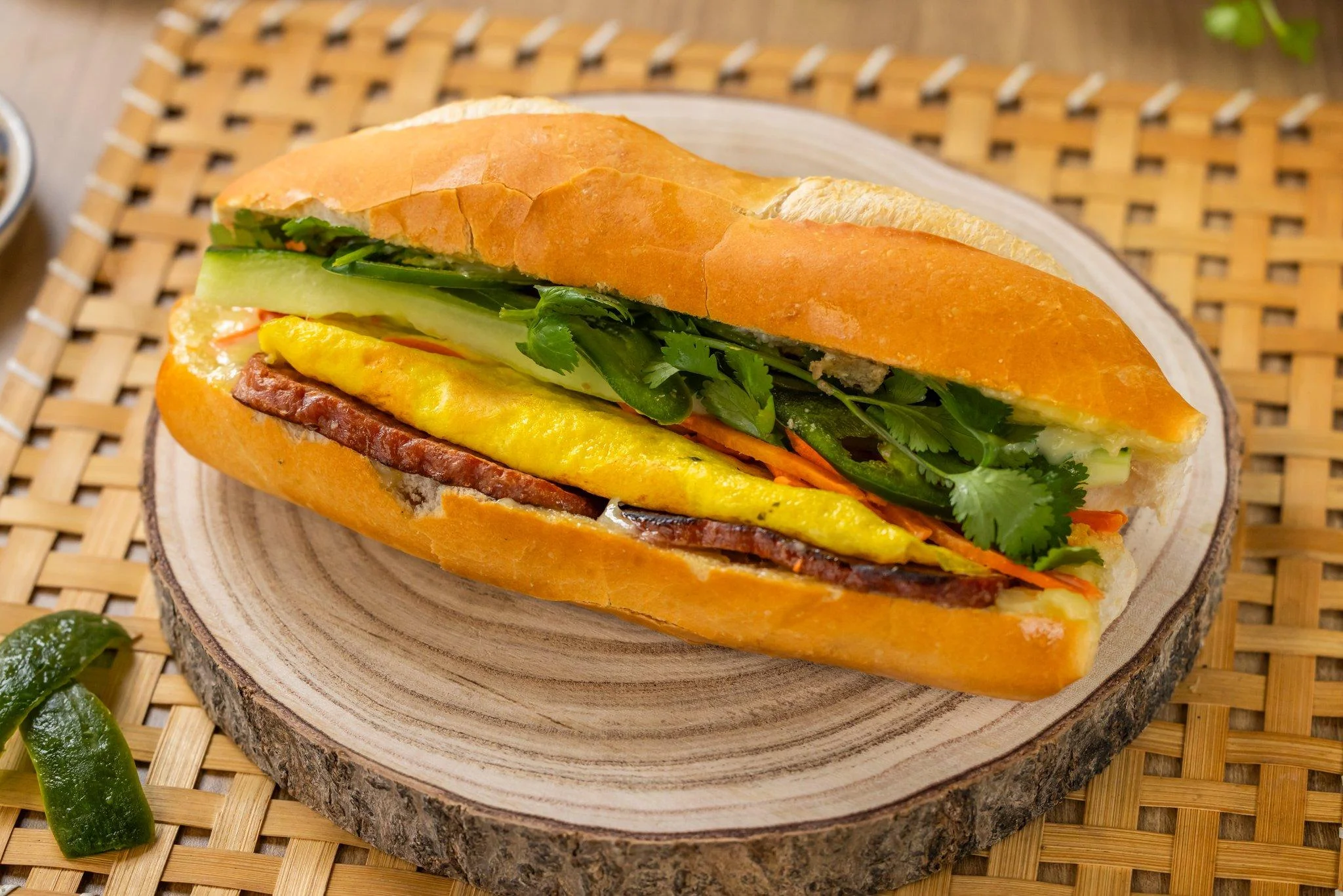 A sandwich featuring a yellow egg omelette, meat, and fresh veggies, all nestled in a baguette.