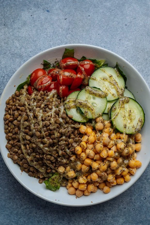 A nutritious bowl featuring lentils, chickpeas, cherry tomatoes, cucumber slices, and leafy greens, all drizzled with a light dressing.