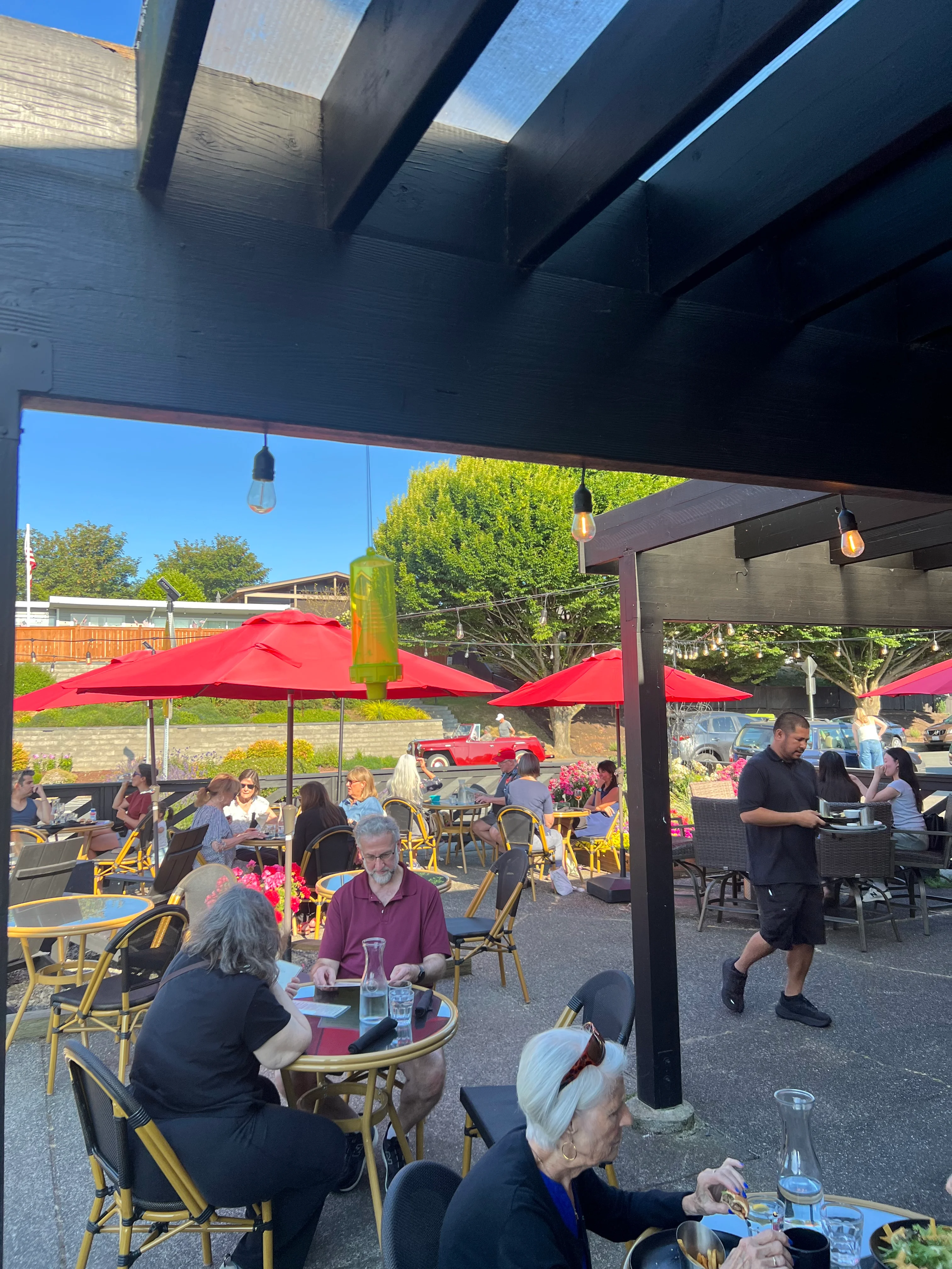 Outdoor dining area with red umbrellas and patrons enjoying their meals