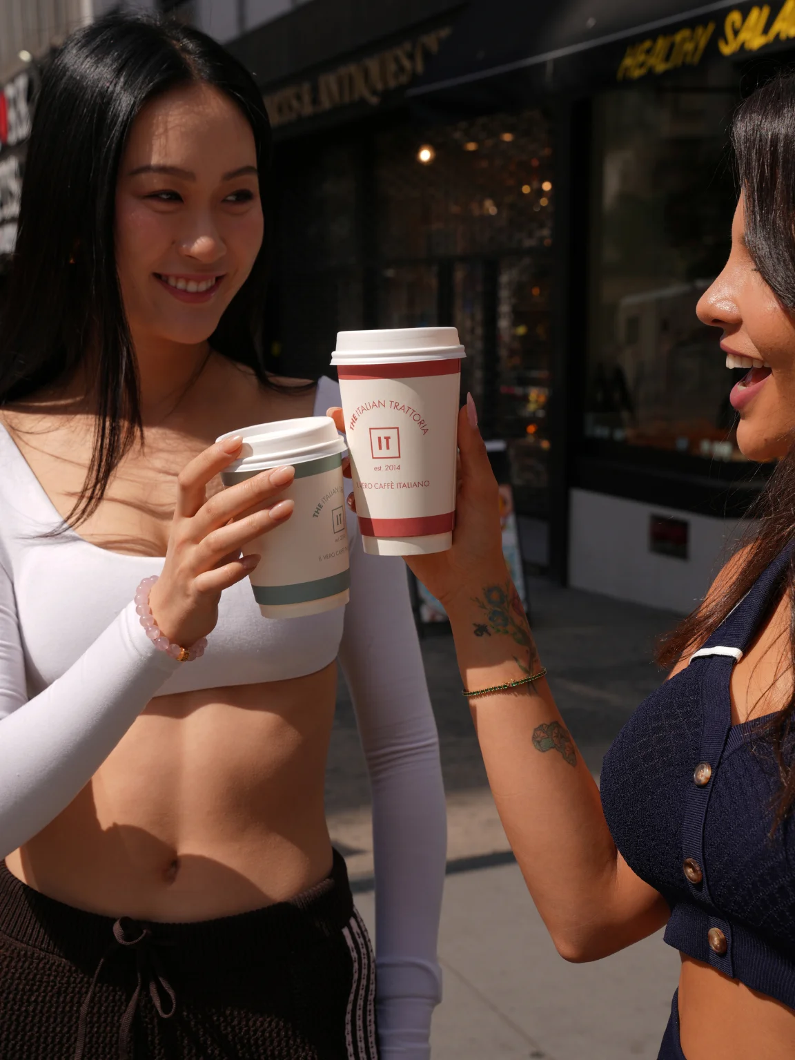 Two friends toasting coffee cups outside a café