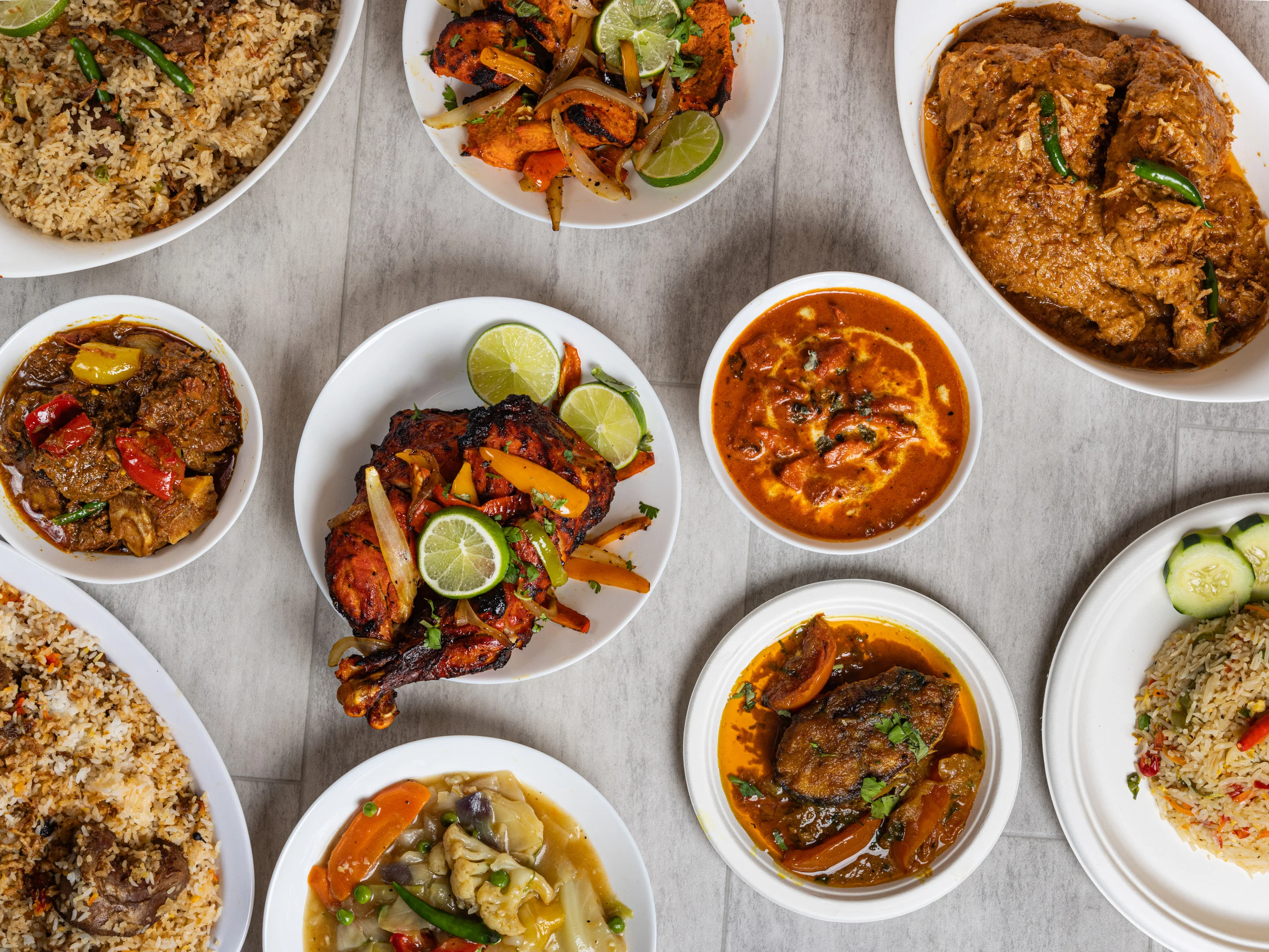 A variety of dishes served on white plates, including chicken, curry, rice, and vegetables, garnished with herbs and lime.
